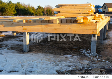 Lumber and beams for wooden house, stacked near foundation, site material preparation, timber construction, carpentry supplies, building stock, project start. Lumber and beams for wooden house, stacked near foundation, site material preparation, timber construction, carpentry supplies, building stock, project start. 138435450