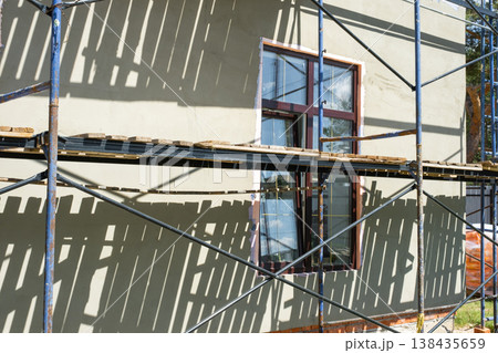 Leveling plaster layer on facade, scaffolding erected for wall insulation, finishing works, render application, house improvement, protective coating system. Leveling plaster layer on facade, scaffolding erected for wall insulation, finishing works, render application, house improvement, protective coating system. 138435659
