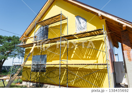 Painting facade plaster, construction scaffolding, exterior wall finish, decorative timber boards, half-timbered design, house renovation, final construction step. Painting facade plaster, construction scaffolding, exterior wall finish, decorative timber boards, half-timbered design, house renovation, final construction step. 138435692