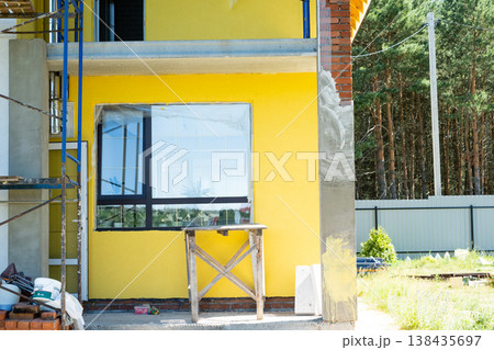Yellow facade paint on house, over plaster layer, decorative wood elements (if present), final wall finish, external renovation, architectural detail, scaffolding visible. Yellow facade paint on house, over plaster layer, decorative wood elements (if present), final wall finish, external renovation, architectural detail, scaffolding visible. 138435697