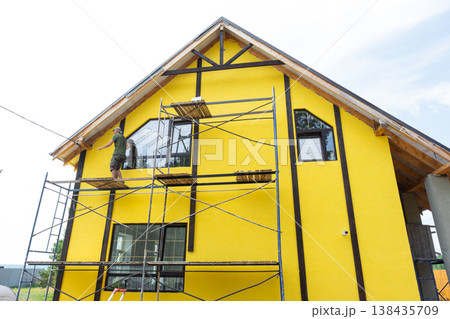 Finished house facade, exterior yellow paint over plaster, decorative timber boards, half-timber framing, wall protection, modern construction, final cladding stage. 138435709