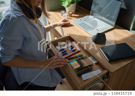 Woman arranging office supplies in open desk drawer beside laptop on desk Woman arranging office supplies in open desk drawer beside laptop on desk 138435719