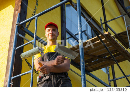 Smiling builder portrait, paint roller, facade painting, maintenance, home repair service, ladder, improvement, professional team, customer call, toolkit. Smiling builder portrait, paint roller, facade painting, maintenance, home repair service, ladder, improvement, professional team, customer call, toolkit. 138435810