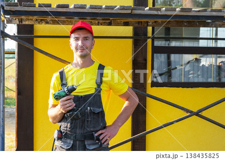 Portrait of builder with drill in overalls, building new house, private handyman business, do-it-yourself work, home improvement, tool expert, client visit. Portrait of builder with drill in overalls, building new house, private handyman business, do-it-yourself work, home improvement, tool expert, client visit. 138435825