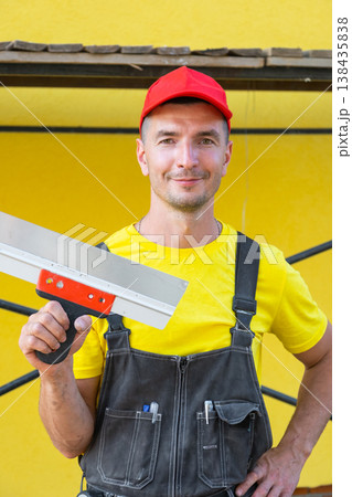 Handyman in yellow, holding large putty knife, at-home repairs, private construction business, do-it-yourself home improvement, professional tool setup. Handyman in yellow, holding large putty knife, at-home repairs, private construction business, do-it-yourself home improvement, professional tool setup. 138435838