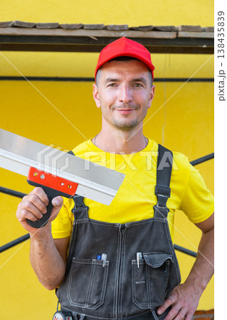 Builder portrait with putty knife, plastering repairs, home renovation business, craftsmanship in finishing works, tools for at-home maintenance. 138435839