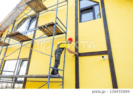 Skilled exterior builder attaches wooden beams in half-timber style, decorative house facade, home improvement, construction, expert renovation work. 138435894