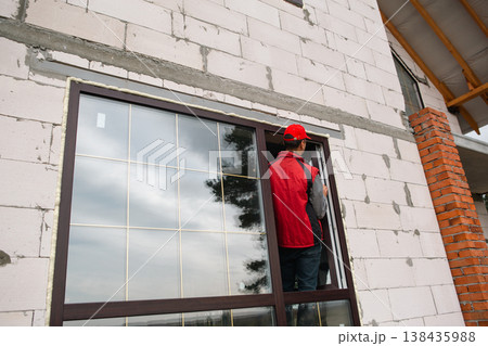 Window installer works on PVC frame placement in new house, accurate alignment and adjustment, professional service for modern home installation business. Window installer works on PVC frame placement in new house, accurate alignment and adjustment, professional service for modern home installation business. 138435988