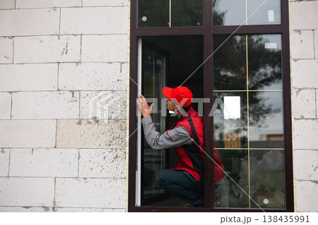 Worker regulates newly installed plastic window at home, ensures sealing and alignment, quality control by professional window installer, home renovation. Worker regulates newly installed plastic window at home, ensures sealing and alignment, quality control by professional window installer, home renovation. 138435991