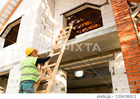 Builder positions ladder for roof access, starts masonry tasks, site setup, safety briefing for team, bricklaying, construction process, home project. 138436021