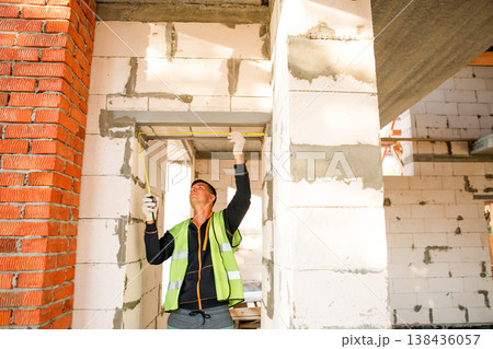 Builder fastens joint, installs support, checks wall frame setup, site action, supervision, teamwork, technical solutions, improvement, home building, mounting. Builder fastens joint, installs support, checks wall frame setup, site action, supervision, teamwork, technical solutions, improvement, home building, mounting. 138436057