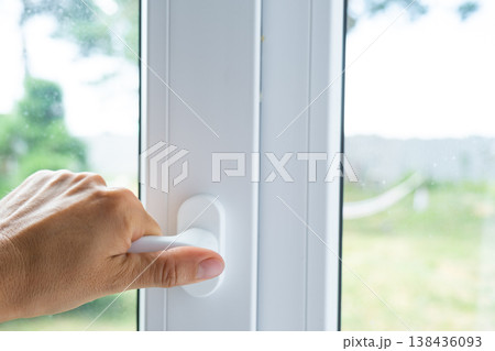 Plastic window being opened with a white handle, premium hardware, setup for comfortable airing, sound insulation, anti-draft features, and business installation. 138436093