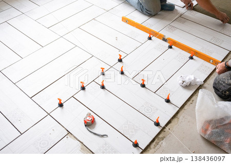 Laying floor tiles diagonally, use of spacers and level, tiling process in progress, professional renovation, tools for accurate tile alignment. Laying floor tiles diagonally, use of spacers and level, tiling process in progress, professional renovation, tools for accurate tile alignment. 138436097