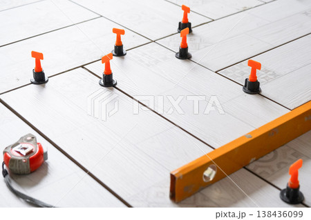 Floor tiling in progress, ceramic tiles with spacers and leveling system, repair and renovation work, home improvement, professional installation tools. 138436099