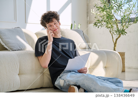 Young handsome guy, 20s university student talking on cell phone with paper documents Young handsome guy, 20s university student talking on cell phone with paper documents 138436649