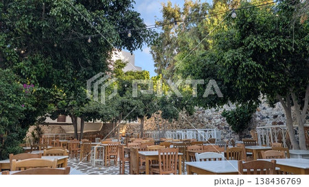 Many tables and chairs in an outdoor restaurant surrounded by stone walls and trees in the old town 138436769