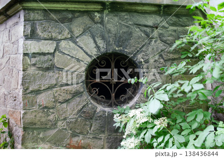 Historic Stone Building With Ornate Circular Window Surrounded By Lush Green Foliage And Delicate White Flowers In A Serene Outdoor Setting 138436844