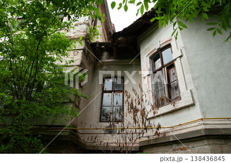 Weathered Historic Building Facade Overgrown With Green Trees And Dead Vines Showing Peeling Paint And Old Windows In Natural Light Weathered Historic Building Facade Overgrown With Green Trees And Dead Vines Showing Peeling Paint And Old Windows In Natural Light 138436845