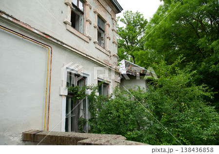 Weathered Two-Story Building With Peeling Paint And Overgrown Green Foliage Surrounded By Lush Trees In A Quiet Rustic Setting Weathered Two-Story Building With Peeling Paint And Overgrown Green Foliage Surrounded By Lush Trees In A Quiet Rustic Setting 138436858