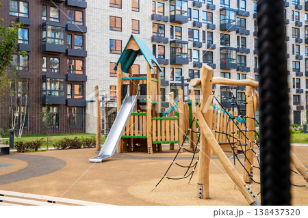 Wooden playground with slide in residential courtyard. Outdoor recreational complex for child activity near modern apartment building. Urban leisure infrastructure for kids development. 138437320