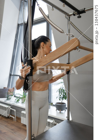 Fitness woman gripping pilates spring bar with two hands, preparing for reformer routine indoors. Spring bar, reformer, pilates, grip, fitness routine. Fitness woman gripping pilates spring bar with two hands, preparing for reformer routine indoors. Spring bar, reformer, pilates, grip, fitness routine. 138437675