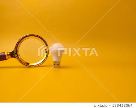 A minimalist studio shot featuring a golden magnifying glass placed next to a small white USB LED light bulb. A minimalist studio shot featuring a golden magnifying glass placed next to a small white USB LED light bulb. 138438064
