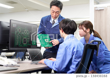 電子基板を手に持ち回路構成と制御コードを確認し合う工場系ITチームの開発現場 138438168