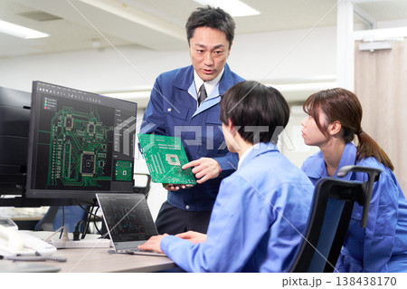 実機基板とモニターを見ながらプログラミングを行う技術者たち 138438170