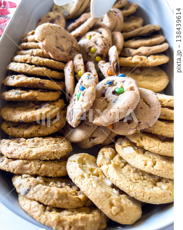 White serving tray filled with various types of cookies including chocolate chip and sprinkle-covered cookies. The cookies are stacked in neat rows and surrounded by soft lighting. White serving tray filled with various types of cookies including chocolate chip and sprinkle-covered cookies. The cookies are stacked in neat rows and surrounded by soft lighting. 138439614