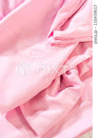Light pink bed sheet appears partially folded and wrinkled on a light surface. Fabric texture and loose folds are clearly visible. 138439617