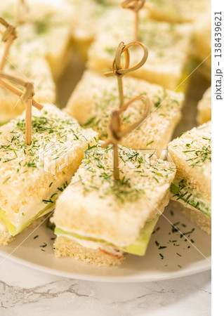Delicate mini cucumber sandwiches made with soft white bread, layered with a creamy dill-flavored spread and thin slices of cucumber, secured with bamboo cocktail picks. Ideal for tea parties, bridal Delicate mini cucumber sandwiches made with soft white bread, layered with a creamy dill-flavored spread and thin slices of cucumber, secured with bamboo cocktail picks. Ideal for tea parties, bridal 138439621