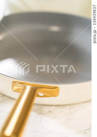 A sleek ceramic frying pan with a golden handle displayed on a marble surface. Ideal for product pages, cooking gear promotion, or kitchen design inspiration. A sleek ceramic frying pan with a golden handle displayed on a marble surface. Ideal for product pages, cooking gear promotion, or kitchen design inspiration. 138439637