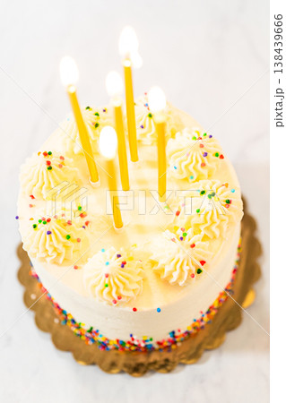 A top-down view of a round frosted birthday cake with five lit candles placed evenly on top. The cake is decorated with piped frosting swirls and sprinkles, set on a white background. 138439666