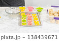 A baking tray filled with colorful flower-shaped cookies coated in yellow, pink, and green sugar, part of the Easter Cookie Sandwich with Raspberry Buttercream recipe. 138439671