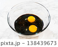 A bowl filled with molasses and two large eggs for Spiced Gingerbread Cookie Dough Perfect for Baking. The dark molasses contrasts with the bright yolks, creating a rich base for the dough. 138439673