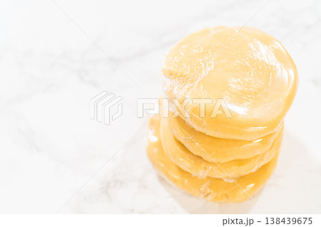 Close-up view of Classic Sugar Cookie Dough wrapped in plastic wrap, prepared for chilling in the refrigerator. This step ensures the dough firms up, making it easier to roll and cut for baking. 138439675