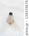 A single metal piping tip is isolated on a white marble surface. Bright lighting highlights clean shape and baking tool detail. 138439678