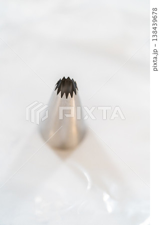 A single metal piping tip is isolated on a white marble surface. Bright lighting highlights clean shape and baking tool detail. A single metal piping tip is isolated on a white marble surface. Bright lighting highlights clean shape and baking tool detail. 138439678