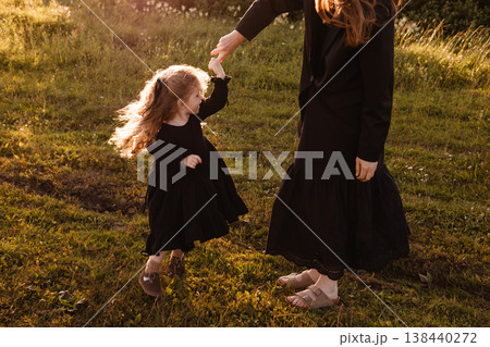 Child Spins Joyfully As Mother Guides. Sunlit Hair Dances As Mother Leads Playful Daughter Child Spins Joyfully As Mother Guides. Sunlit Hair Dances As Mother Leads Playful Daughter 138440272