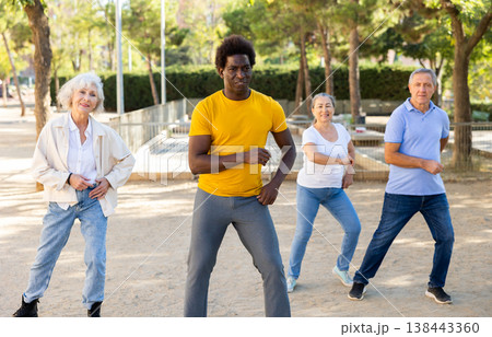 Active mature women and men learning modern dynamic dances in summer park Active mature women and men learning modern dynamic dances in summer park 138443360