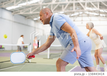 Aged man playing friendly pickleball match on indoor court 138443414
