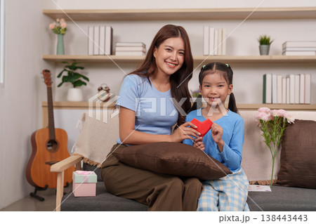 Mother and daughter exchanging a heart-shaped gift Mother and daughter exchanging a heart-shaped gift 138443443
