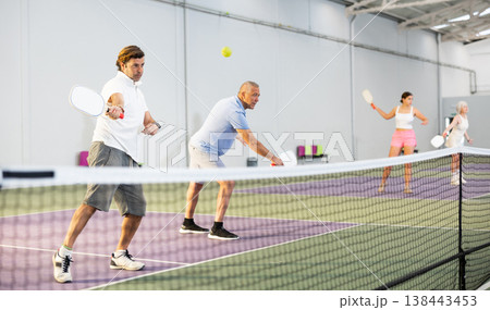 Focused adult man playing pickleball match in team with older partner Focused adult man playing pickleball match in team with older partner 138443453