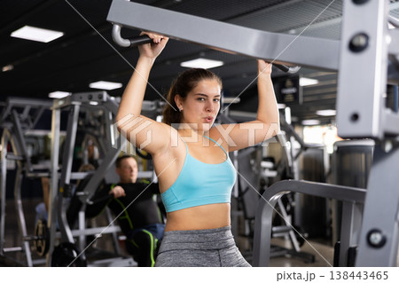 Girl training back muscles in lat pull-down lever machine Girl training back muscles in lat pull-down lever machine 138443465