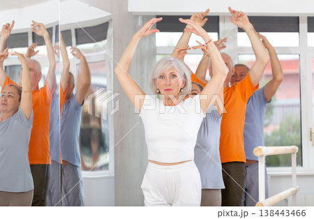 Active mature woman practicing fifth position holding by ballet barre together with others Active mature woman practicing fifth position holding by ballet barre together with others 138443466