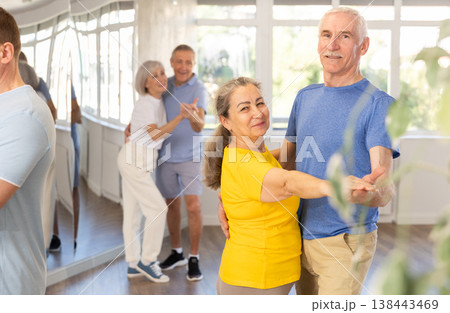 Group of elderly pensioners learn to dance a couple tango dance in dance class 138443469