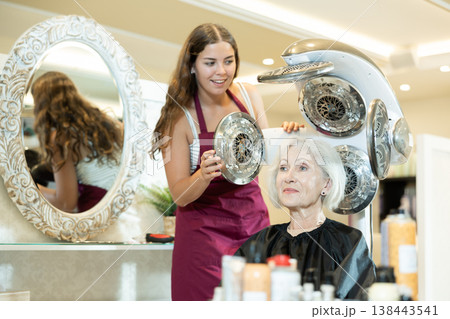 Young female hairdresser adjusting settings of thermostimulator for elderly woman Young female hairdresser adjusting settings of thermostimulator for elderly woman 138443541