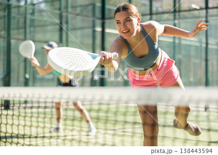 Young sporty woman playing padel game in court on sunny day Young sporty woman playing padel game in court on sunny day 138443594