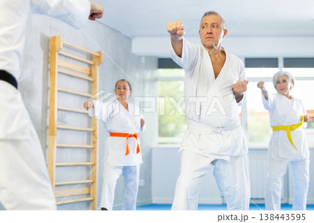 Old man attendee of karate classes practicing kata standing in row with others 138443595