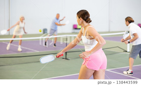 Rear view of young woman playing pickleball on indoor court Rear view of young woman playing pickleball on indoor court 138443599